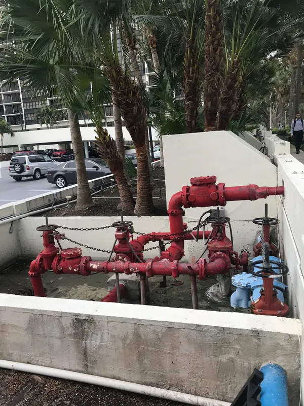 Large red commercial backflow preventer assemblies with blue valves installed in a walled enclosure outside a Miami condominium.