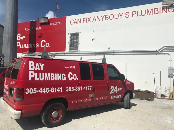Red Bay Plumbing Co. service van marked 24 hrs service, parked at the shop under a wall painted Can fix anybody's plumbing.
